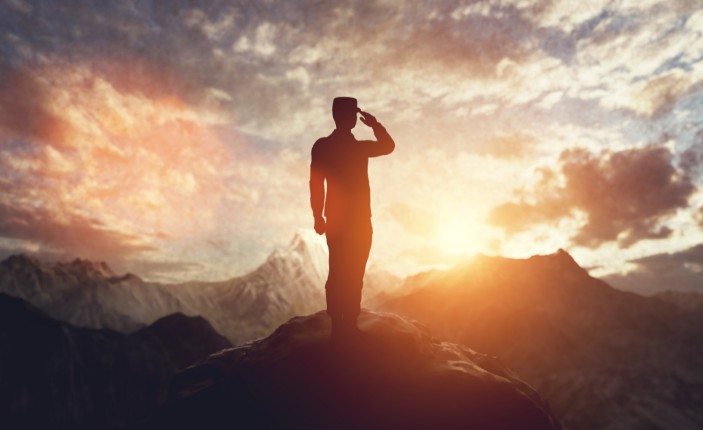military service member saluting on mountaintop clouds and sunset background