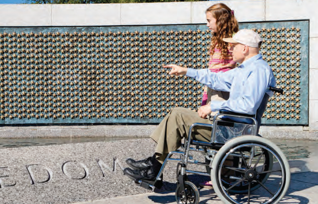 World War ll veteran in wheelchair with daughter looking at Freedom Wall