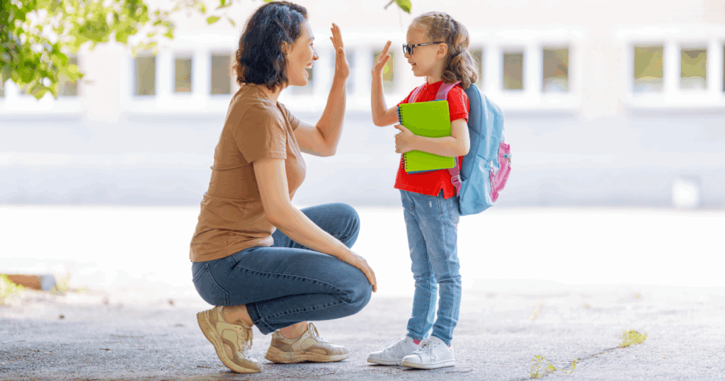 Mom and daughter wearing backpack high five outside school
